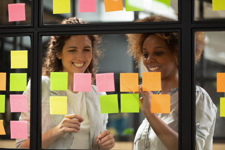 reative young female coworkers having fun planning project write on sticky notes glass wall